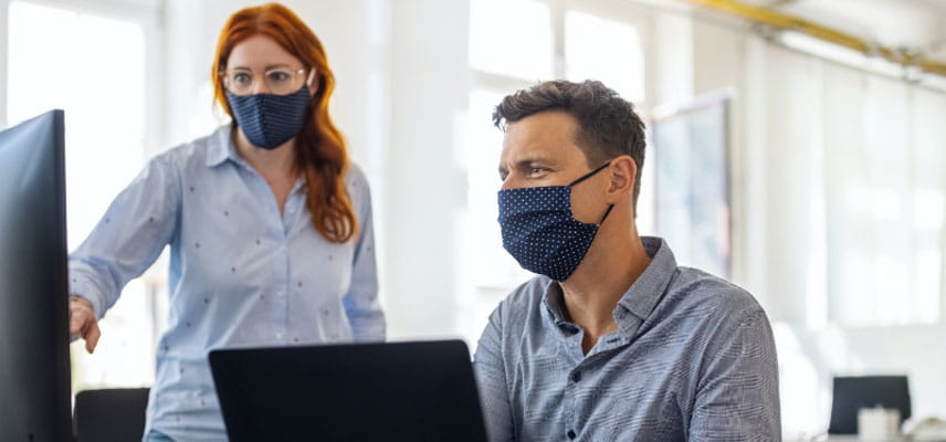 man and woman at computers wearing face masks