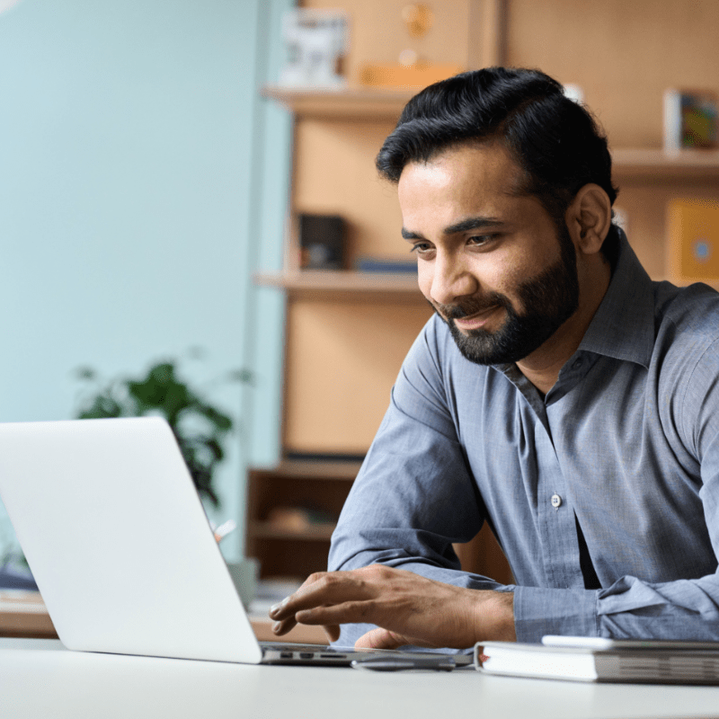 A man is looking at a laptop device while sitting at a desk.