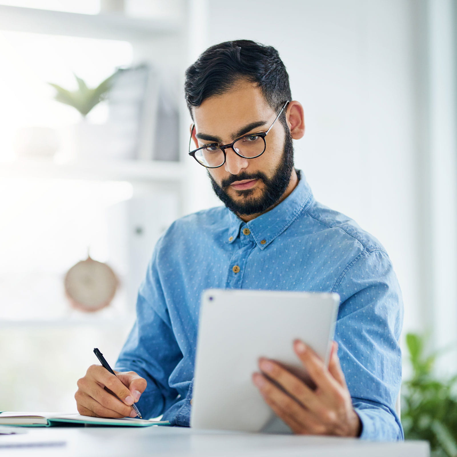 Man at desk taking notes holding an ipad